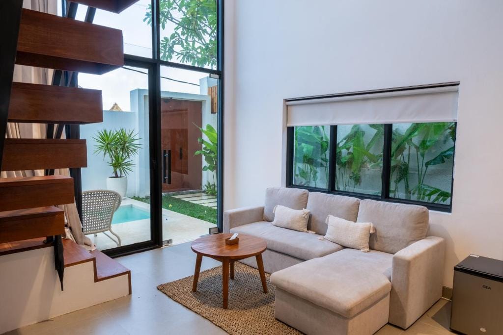 Living room with an open timber stair, looking through full-height glass to a private plunge pool