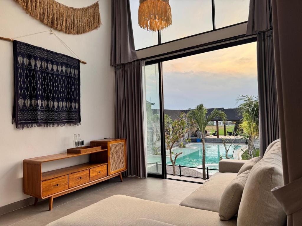 Villa living room with a teak sideboard and a woven ikat textile on the wall, opening onto the resort pool at dusk