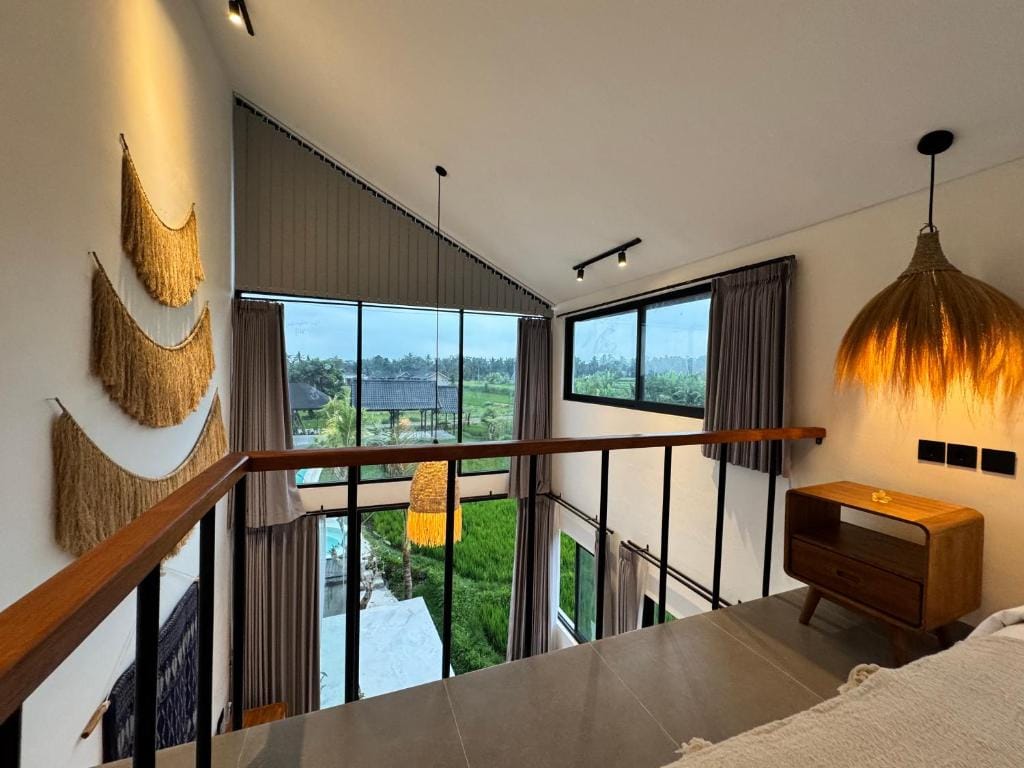 View from a villa mezzanine down through double-height windows to the pool and the rice fields beyond